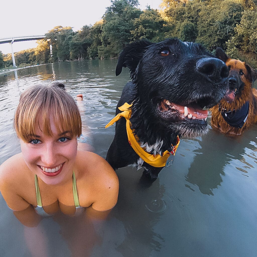 Blair and Mia, a black dog, are in the river. Mia's nose points towards the camera as Blair smiles.