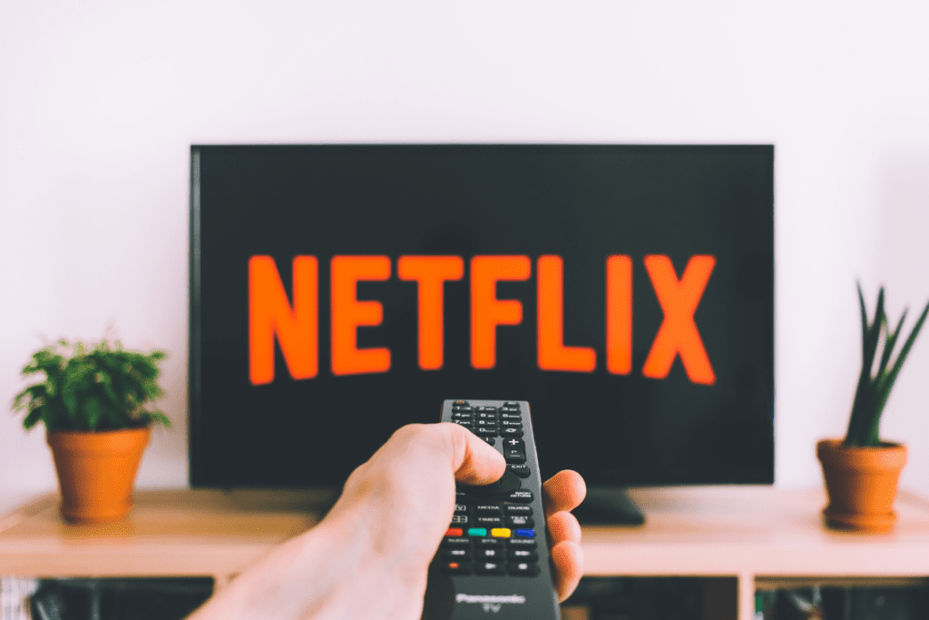 hand holds a remote in front of a tv screen with netflix on it